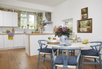 Open-plan kitchen and dining area with wooden floorboards, botanical wallpaper and vintage oil paintings.