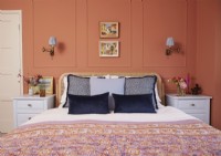 Bedroom with terracotta painted panelling, fitted wall lights and vintage oil paintings.