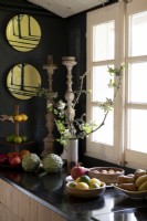 Wall mounted plates on black wall next to bowls of fruit in kitchen