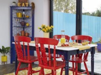 Open-plan dining area detail with red painted chairs and a yellow spotty rug.
