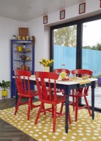 Open-plan dining area with red painted chairs and a yellow spotty rug.