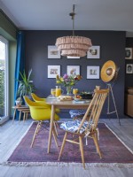 Open plan dining area with yellow vintage style chairs, a patterned rug and dark blue painted walls.