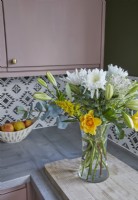 Kitchen detail showing worktop with a vase of flowers, pink cabinets and patterned tiling.