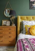Bedroom detail showing yellow double bed, wooden vintage drawers and green painted walls.