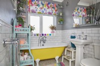Colourful bathroom with yellow freestanding bath, white metro tiles and grey walls.