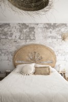 Bare plaster wall behind bed with rattan headboard