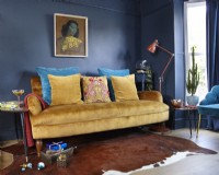 Living room with a mustard yellow sofa, 'The Green Lady' print, navy painted wall, retro side tables and Christmas presents.