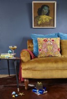 Living room detail with a mustard yellow sofa, 'The Green Lady' print, navy painted wall and retro side tables with Christmas presents.