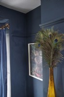 Living room detail showing decorative peacock feathers in a vase, retro artwork and navy blue painted walls.