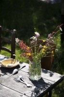 Wildflower arrangement in old glass jar on garden table
