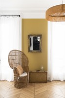 Wicker chair next to mustard painted wall in bedroom