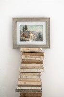 Detail of framed painting supported by a tall pile of books 