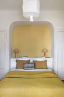 Yellow painted alcove above bed in white bedroom
