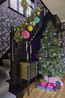 Christmas hallway with a decorated tree and presents. Black painted bannister and wallpaper going up the stairs.