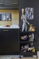 Kitchen detail showing dark brown cabinets, gold wallpaper and a drinks trolley with a monkey light.
