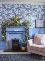Living room detail showing a mantlepiece decorated for Christmas, jungle print wallpaper and blue panelling.