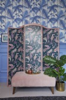 Living room detail showing a patterned screen, jungle print wallpaper and blue panelling.