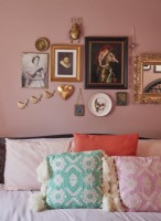 Bedroom detail showing bed with textured cushions and a pink gallery wall with gold accents.