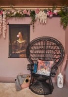 Bedroom detail showing a black peacock chair, flower decorations and artwork on the pink painted walls.