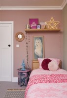 Bedroom with pink walls, a wallpapered side table and retro artwork.