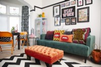 Colourful living room with green sofa, orange footstool and a gallery wall.