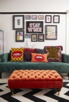 Colourful living room with green sofa, orange footstool and a gallery wall.
