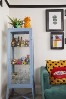 Colourful living room detail showing a glass cabinet filled with ornaments and green sofa.