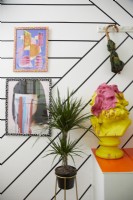 Entrance detail showing yellow head sculpture, plant, framed artwork, washi tape stripe walls and an umbrella hanging on coat hooks.