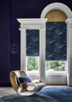 Dark blue opulent living room with gold designer chai in front of patterned roman blinds