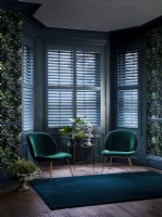 Living room with green chairs, patterned wallpaper and shutters