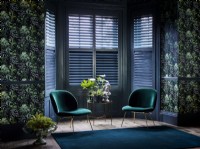 Living room with patterned wallpaper, green chairs and shutters