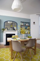 Open plan kitchen-diner with blue walls, a victorian fireplace and a yellow rug.