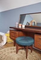 Bedroom detail showing a mid-century dressing table, teal stool and blue painted walls.
