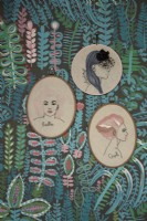 Living room detail showing framed embroideries of women's faces woth patterned wallpaper.