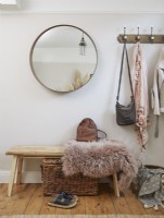 Entrance detail with coat hooks, a round mirror, a bench, and a wicker storage box.