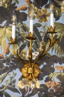 Gold leaf shaped lighting sconce on wall with floral patterned wallpaper.