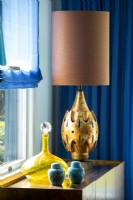 Bronze coloured lamp on table with yellow glass decanter and blue ceramic jars.