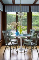 Round white pedestal dining table with wooden chairs and garden view.