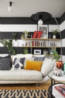 Black and white striped walls in a modern open plan living room space. With a cream leather sofa and patterned rug.