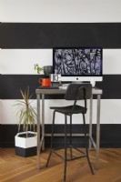 Home office area in an open plan living space. With black and white striped walls, a stool and a plants.