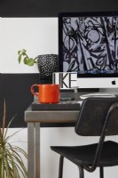 Home office area in an open plan living space. With black and white striped walls, a stool and a plants.