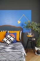 Bold and colourful painted bauhaus shapes in a contemporary bedroom. With an antique headboard, patterned soft furnishing and a yellow anglepoise lamp.