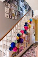 Gallery walls around a staircase decorated with colourful paper pom poms
