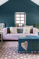 Pink sofa in an attic bedroom with green hand painted decorative chest and a white spotted pink rug