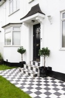 Black and white chequered paving and steps leading to a black front door in a white house