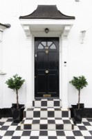 Black and white chequered paving and steps leading to a black front door in a white house