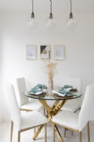 Brass and glass dining table with white upholstered dining chairs