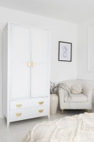 Corner of a white bedroom with freestanding wardrobe and chair 
