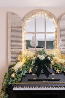 Black upright piano decorated with ivy, feathers and Christmas baubles with a shutter mirror behind