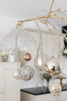 Christmas baubles hanging from a gold sprayed twig between pendant lights in an open plan kitchen diner